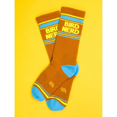 Bird Nerd Unisex Socks by Gumball Poodle: brown wide ribbed socks with blue toes and heels, yellow and blue stripes, and “BIRD NERD” in yellow near the top, shown on a bright yellow background.