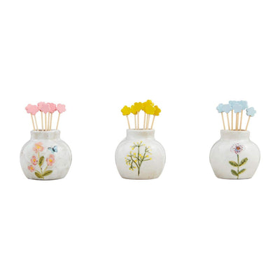 The Botanica Toothpick Caddy Set from Mud Pie includes three small white ceramic vases with intricate hand-painted floral designs, each holding colorful cocktail picks with flower-shaped tops in pink, yellow, and blue for an elegant display.