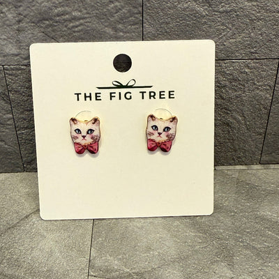A pair of Bowtie Kitty Post Earrings by Golden Stella, featuring 1/2 long cat shapes with pink bows and gold-dipped brass base, displayed on a white The Fig Tree card against a gray textured background.