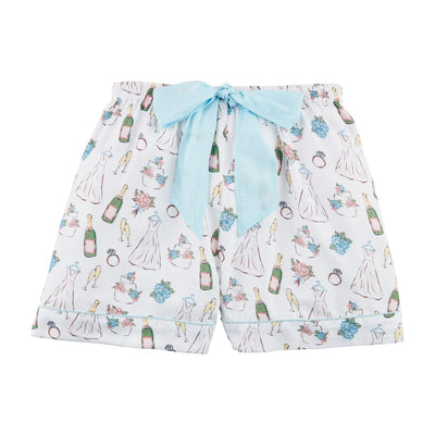 The Mud Pie Bride Pajama Shorts are white polyester with a pattern of champagne bottles, bridal dresses, rings, and bouquets. They feature a light blue ribbon at the elastic waist and convenient side pockets for added functionality.