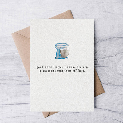 The Good moms let you lick the beaters Mothers Day card by La Nouille Studio features a matte illustration of a blue stand mixer with the humorous text and comes elegantly paired with a kraft envelope on a wooden surface.