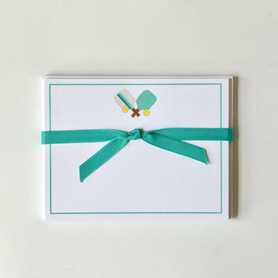 Pickleball Flat Note Cards by Georgetown Paperie: ultra white cards with a teal border, pickleball paddles and balls at top center, tied with a teal ribbon. Envelopes included.