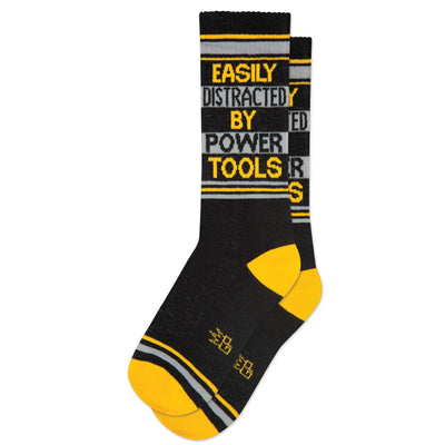 Gumball Poodle's Easily Distracted By Power Tools Gym Crew Socks feature black and yellow stripes with the phrase “EASILY DISTRACTED BY POWER TOOLS” across the top.