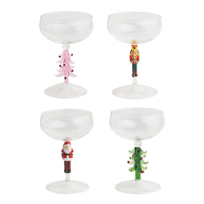Set of four Mud Pie Christmas Coupe Glasses, each 6.5 oz, featuring festive figural stems with a pink Christmas tree, nutcracker, Santa Claus, and green Christmas tree, arranged in two rows on a white background.
