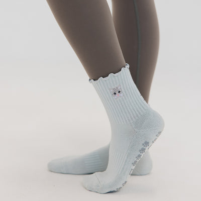 A person wears Almla Active Meow Pilates Socks—women’s gray and light blue ribbed socks with cat faces, scalloped edges, heart paw print grips, and charming non-slip features.