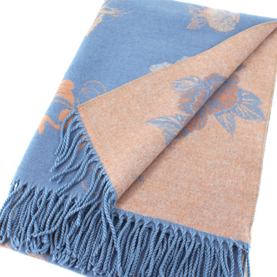 The Pamelina Scarf by Pretty Persuasions is a folded, fringed accessory made from soft viscose and durable polyester with a blue side featuring an orange floral pattern and an orange reverse with blue florals. One corner is turned to show both sides.