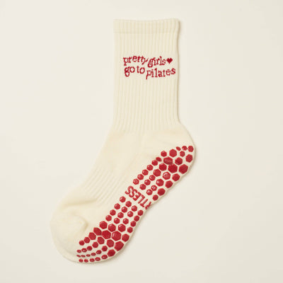 The Effortless Club Pilates Girl Grip Sock in Red is a white ribbed organic cotton sock with red non-slip grips on the sole and pretty girls go to pilates text with heart accents on the cuff.