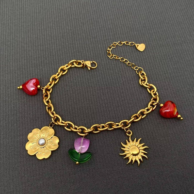 The Mio Queena Sun, Flower & Heart Charm 18K Gold Plated Bracelet features two red hearts, a gold flower with pearl center, a green-purple butterfly, and sun charm on non-tarnish stainless steel.