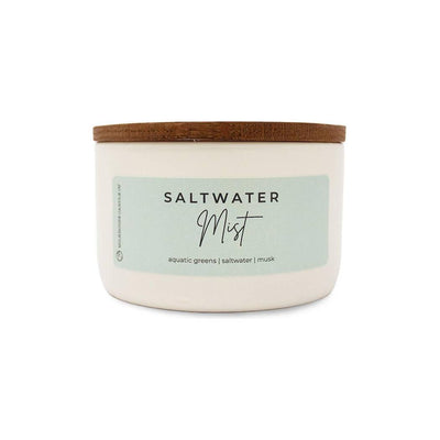 The Milkhouse Candle Company Saltwater Mist Statement Candle is a white natural soy wax jar with a wooden lid and a soft mint green label, featuring aquatic greens, saltwater, and musk notes for an inviting beach scent.