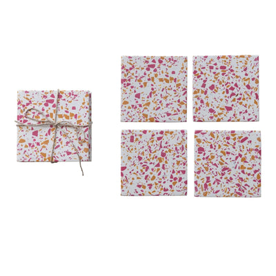 Against a white background, the Creative Co-op Resin Terrazzo Coasters, Set of 4, feature a pink, orange, and white pattern. On the left, a similar set is elegantly tied with thin string.