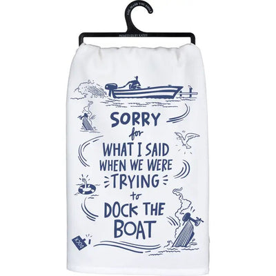 The Primitives by Kathy Trying To Dock the Boat Kitchen Towel is a white, machine washable cotton towel with navy blue illustrations of people docking a boat and the humorous text, SORRY for WHAT I SAID WHEN WE WERE TRYING to DOCK THE BOAT. Its dimensions fit perfectly into any kitchen decor.