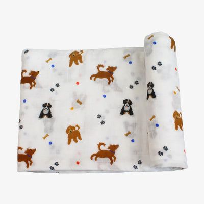 The Bamboo Little Dogs Swaddle is a soft white cotton muslin baby blanket featuring playful brown and black dogs, bones, paw prints, and colorful dots. One side of this charming Dogs Swaddle is shown neatly rolled up.