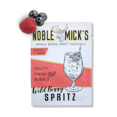 A packet of NOBLE MICKS Wild Berry Spritz Single Serve Craft Cocktail is shown with a cocktail glass illustration, fresh blueberries, and a raspberry above it. The packaging highlights fruity, fresh, bubbly craft cocktails.