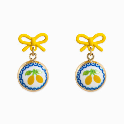The Sessori Ceramic Lemon Pop Bow Earrings feature yellow bow studs and round, gold-framed pendants displaying illustrated lemons with green leaves on a white background.