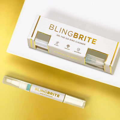 The Bride Brite BlingBRITE On-The-Go Ring Cleaner set features a white and gold box with bold lettering and a clear pen-like cleaning brush, displayed on a white and yellow background for quick jewelry shine.