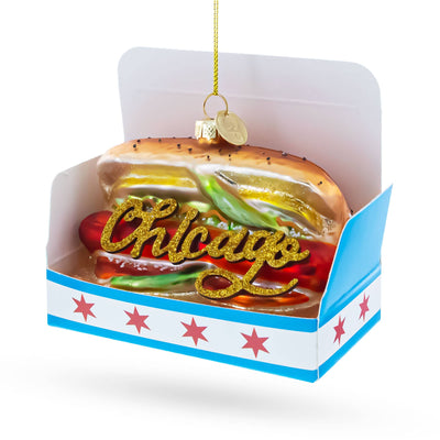 The BestPysanky Chicago Style Hot Dog Glass Ornament features glittery “Chicago” text and hangs from a gold string, packaged in a blue and white box with red stars.