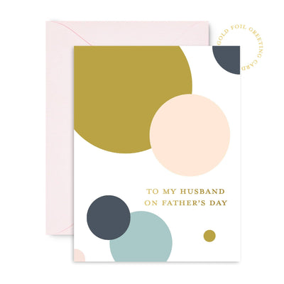 Sublime & Co.s To My Husband On Fathers Day Card features a minimalist design with gold, peach, teal, and gray circles. The card has gold foil text on premium paper and includes an off-white envelope for elegance.