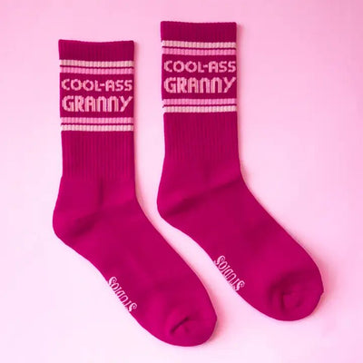 Sunshine Studios Cool Ass Granny Ribbed Crew Socks are bright pink with Cool-Ass Granny white text on a matching background, featuring Socks at the bottom, showcasing quality and sustainability in ethically sourced packaging. Made from organic cotton.