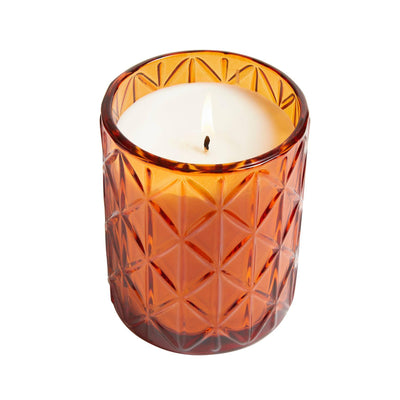 A lit Hillhouse Naturals/Field+Fleur Spiced Pumpkin Large Glass Candle (15oz) in a textured amber diamond-patterned holder, set against a white background.