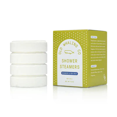 Four round white Seaweed & Sea Salt Shower Steamers by Old Whaling Company are stacked beside a yellow and white box, featuring clear product details and an ingredient list on the packaging for a spa-like experience.