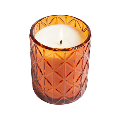 The Hillhouse Naturals Field+Fleur Fallen Leaves Large Glass Candle (15oz) features a decorative textured amber glass holder with a geometric pattern and long burn time, shown on a white background.