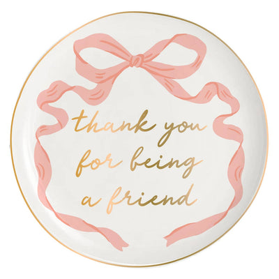 The Bow Thank You For Being A Friend Round Trinket Tray by soiree-sisters is a decorative white ceramic dish with a pink bow design and gold text—ideal as a charming jewelry holder or thoughtful gift for a friend.