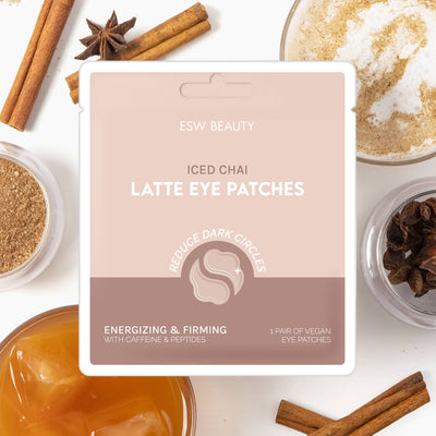 The ESW Beauty Iced Chai Latte Energizing & Firming Eye Patches in a square box are shown on a white background with chai spices, frothed milk, and iced chai—ideal for reducing under-eye dark circles and puffiness.