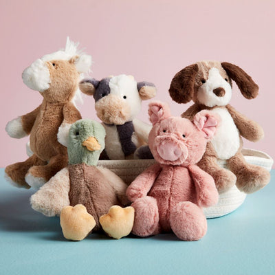 The Mud Pie Farm Plush Rattle Pals, featuring a horse, cow, dog, duck, and pig made with soft faux fur, are displayed in and around a white basket. The pastel pink and light blue background adds to the playful and gentle atmosphere.