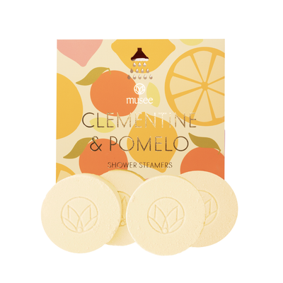 A box of Musee Clementine & Pomelo Shower Steamers features citrus-themed packaging and displays four round, pale yellow steamers infused with a refreshing citrus scent in front of the box.