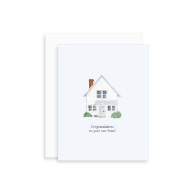 The Korynne and Company Congratulations on Your New Home Greeting Card features a watercolor house with a brown chimney, green bushes, and “Congratulations on your new home!” printed beneath the illustration.