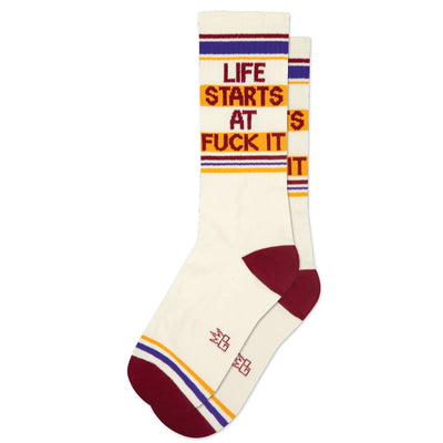 The Gumball Poodle Life Starts At Fuck It Gym Crew Socks are cream-colored unisex socks with maroon heels and toes, purple and yellow stripes, bold calf text, and are made in the USA.
