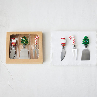 Creative Co-op Cheese Knives with Hand-Blown Glass Holiday Icon Handle feature stainless steel blades and festive handles shaped like Santa, a Christmas tree, and a candy cane—packaged left, displayed right.