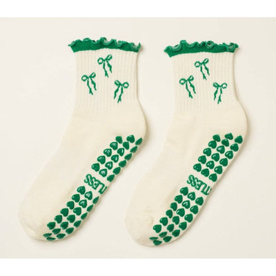 Pair of white socks with green ribbons and patterns on a light beige background