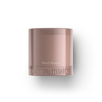 The Hard Wood Essentials Candle by Boy Smells is a beige, translucent jar candle with smoky cedarwood notes and Boy Smells embossed at the base, shown against a white background.