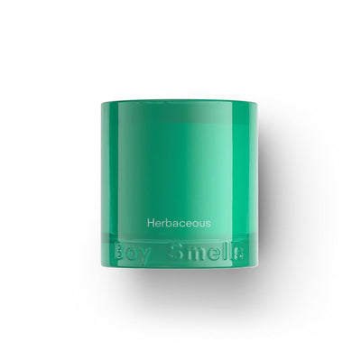 The Boy Smells Herbaceous Essentials Candle features a green glass jar with white labeling and embossed branding, part of the Farm to Candle collection. It offers fresh notes like bergamot sage and is shown against a plain white background.