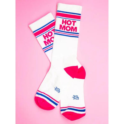 The Gumball Poodle Hot Mom Unisex Socks are mid-calf, wide ribbed socks with blue and red stripes, bold red HOT MOM lettering, and bright pink heels and toes, shown on a pink background.