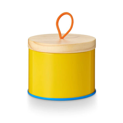 Illume Candles Pool Floatie Sun Tin Candle is a cylindrical yellow container with a wooden lid and bright orange loop handle, topped with a blue-rimmed base and smooth reflective surface that captures light beautifully.