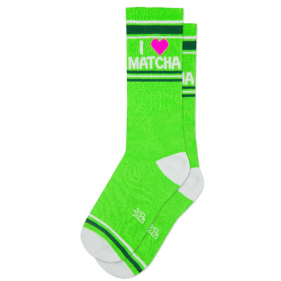 The Gumball Poodle I Heart Matcha Gym Crew Socks are bright green cotton with white heels and toes, dark green stripes, a pink heart with I ♥ MATCHA in white at the top, and small white lettering by the toes. Unisex fit.