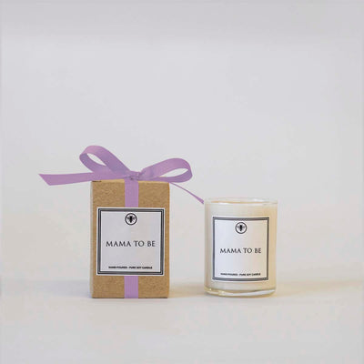A brown gift box with a purple ribbon sits beside the Ella B Candles Mama to Be 3 oz Votive Candle, scented with sweet clover and lavender. Both rest against a plain white background.