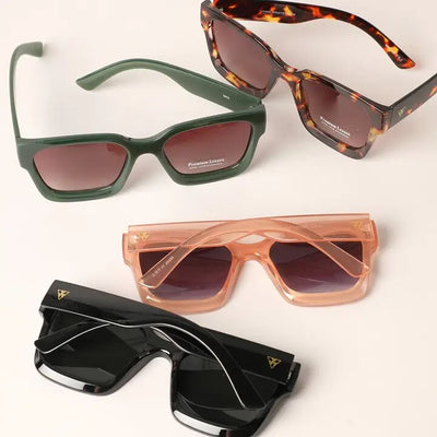 Four pairs of Mathilde Sunglasses by Fashion City are displayed on a neutral background, featuring green, tortoiseshell, pink translucent, and black frames. Each pair boasts oversized square designs with colored gradient lenses and UV protection for optimal eye safety.