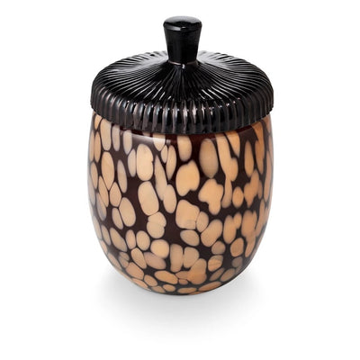The Illume Candles Midnight Pumpkin Glass Acorn Candle is a vegan, plant-based wax candle in an oval jar with a black ridged lid and brown-beige animal print, shown on a white background.