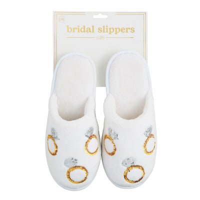 Mud Pies Engagement Ring Bride Slippers, with sequin embroidery on velour and adorned with gold and silver rings, are elegantly presented on a display card. These white bridal slippers feature comfortable rubber soles and add charm to any wedding ensemble.