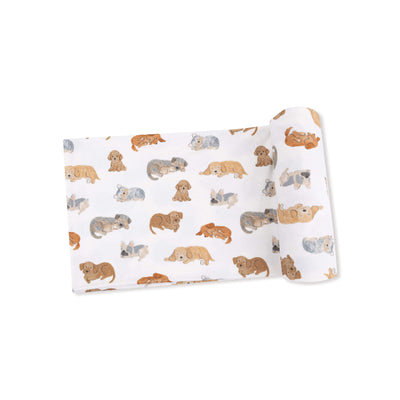 The Napping Puppies Bamboo Stretch Knit Swaddle Blanket by Angel Dear features a soft, rolled-up swaddle with a cute illustrated puppy print in brown, gray, and tan.