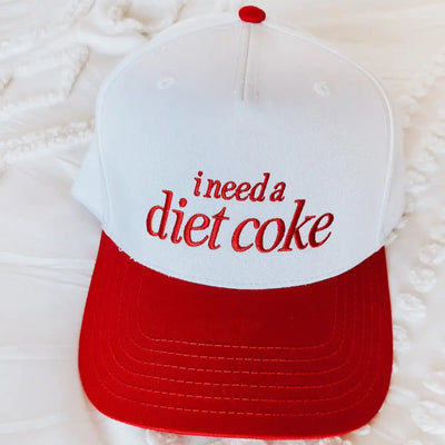 The Maddon and Co I Need a Diet Coke Embroidered Trucker Hat is a white and red unisex adjustable hat featuring “i need a diet coke” stitched in red on the front.
