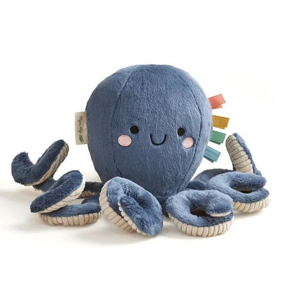 The Octopus Sweetie Snuggles™ Plush by Itzy Ritzy features a blue body, smiling face, and pink cheeks. Its eight curly tentacles have cream-edged tips with colorful ribbon tags for sensory play, and it includes an attached tag.