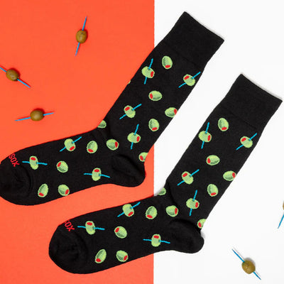 HOTSOX Mens Olives Crew Socks in black (size 6-12.5) feature a green olive and toothpick design, shown on a red and white background with scattered olives on cocktail sticks—an ideal addition to any mens shoe collection.