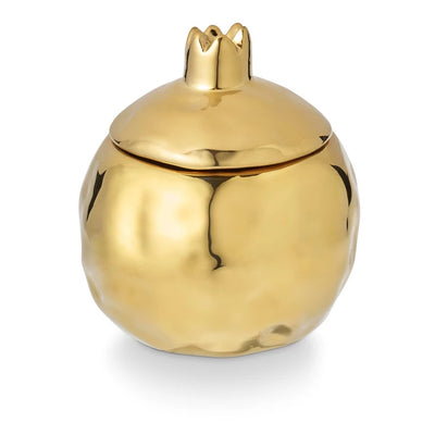 The Illume Candles Pomme Rouge Holiday Fruit Candle features a gold pomegranate-shaped container with a crown-like lid and is crafted from vegan, plant-based wax for an elegant, ethical touch.