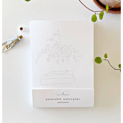 The Potted Plants Paintable Notecards by emily lex studio feature a simple line drawing of a potted plant, ideal for DIY greeting cards or creative watercolor cards. Shown on a white surface with green leaves, a brown pot, and paint tube.