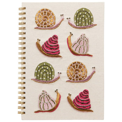 The Danica Studio Gardenland Embroidered Notebook is spiral-bound with a beige cover decorated with six colorful snails—each uniquely embroidered in pink, green, and brown shells—arranged in three rows.
