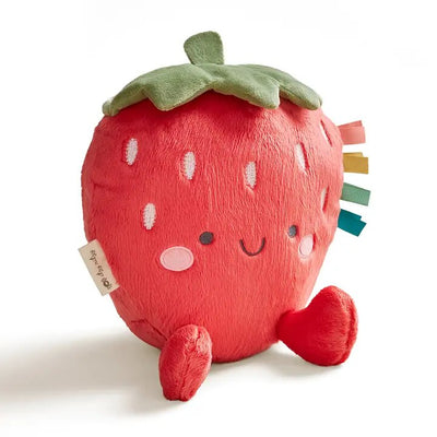 The Itzy Ritzy Strawberry Sweetie Snuggles™ Plush is a strawberry-shaped toy with a smiling face, pink cheeks, and small legs. It features green leaves and colorful fabric tags designed for sensory exploration and a self-soothing experience.